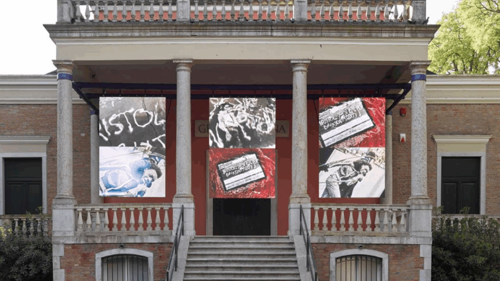 Facade of neoclassical building. Three banners with black-and-white images of police brutality against a black youth hang from the ceiling covering the name inscribed on the building (i.e. Great Britain)